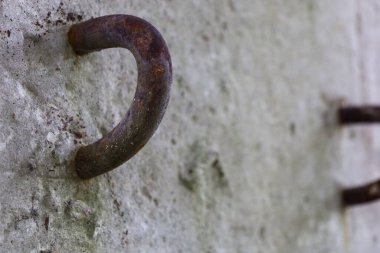 Sert beton bir yüzeye sıkıca gömülmüş paslı bir metal halkanın yakın çekimi. Aşınma metali kırmızımsı kahverengi bir pas tabakasıyla kaplamış. Gri, çatlamış betonla kontrast oluşturmuş..