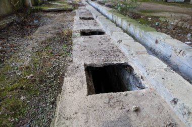 Terk edilmiş beton bir yapı açık kare deliklerle kaplı kirli zemin boyunca yosun ve küçük taşlarla kaplı..