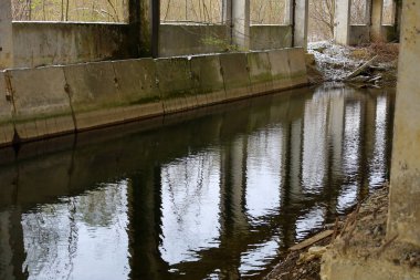 Ukrayna 'da terk edilmiş bir sanayi binasında su basmış beton bir kanal ya da uzun bir su deposu. Sakin su yüzeyi gri beton duvarları, sütunları ve çatının kalıntılarını yansıtır..