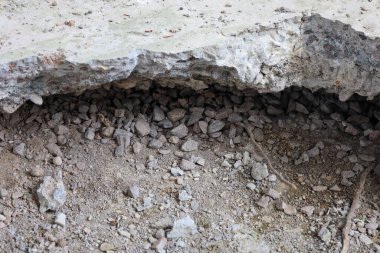 Altındaki kum ve çakıl tabakasını ortaya çıkaran tahrip olmuş beton bir yüzey parçası. Betonun üst katmanı çatlamış ve çatlamış. İç yapısını gösteriyor..