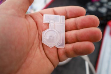 Plastik bir kapakçığı tutan bir elin yakın çekimi. Kapakçığın birkaç bölmesi ve bağlantısı olan karmaşık bir şekli var. Şeffaf madde iç yapıyı görüntülemeye izin verir.