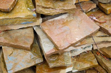 Kahverengi ve sarı tonlarında düz olmayan taş levhaların yakın çekimi. Taşlar düzensiz bir yığının içinde, doğal bir doku oluşturuyor. Bazı tabakalarda nem izleri görülebilir..