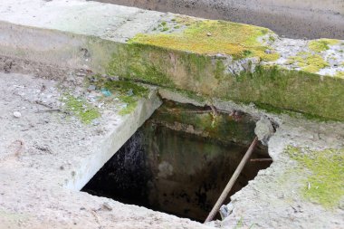 Terk edilmiş bir beton kuyusu ya da yerdeki yosunlarla kaplı bir çukur. Paslı takviye çubukları ve altında karanlık bir boşluk görülebilir.