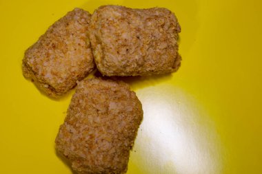 Parlak sarı arka planda üç tane donmuş puf böreği var. Eşyalar düz olmayan, katmanlı açık kahverengi bir dokuya sahip..