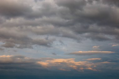 Şiddetli gri yağmur bulutları ile kasvetli gökyüzü, bazı yerlerde ışık kırılır, sıcak sarımsı bir tonda alt katman bulutları renklendirir..