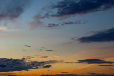Günbatımında akşam gökyüzünün büyüleyici görüntüsü. Koyu mavi ve gri bulutlar güneşin ufukta beliren parlak turuncu ve pembe renkleriyle tezat oluşturur..