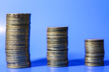 Farklı yükseklikteki üç altın para yığını mavi bir arka fona karşı pürüzsüz mavi bir yüzey üzerinde düzenlenmiştir..