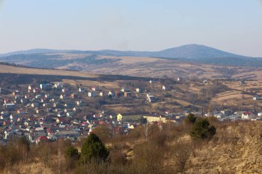 Baharın başlarında Ukrayna 'daki tepelerin arasına yerleşmiş küçük bir kasabanın panoramik manzarası. Ön planda, sarı çimenler ve çalılar görülebilir..