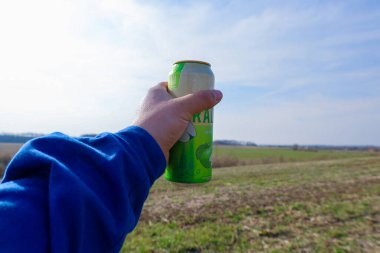 Sambir, Ukrayna - 17 Mart 2025: Fotoğraf, bulanık bir arka plana karşı yeşil bir içecek kutusu tutan mavi kazaklı bir eli gösteriyor.