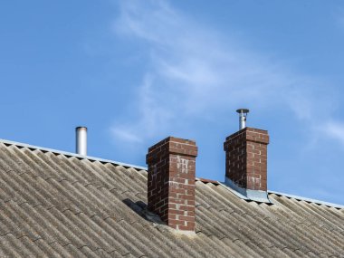 İki tuğladan baca ve bir metal havalandırma borusundan oluşan, açık sirus bulutlu mavi gökyüzü ile kaplı eski bir çatının bir parçası..