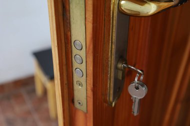 Ahşap kapıya yerleştirilmiş bir anahtarla bir kilidin yakın çekimi. Kilit ve anahtarın metal elementleri ışıkta parlıyor. Doğal ahşap kapının sıcak bir dokusu vardır. Kapı kolunun bir kısmı görünüyor..