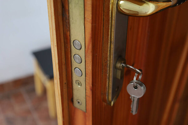 Крупный план замка с ключом, вставленным в деревянную дверь. Металлические элементы замка и ключа мерцают в свете. Дверь из натурального дерева имеет теплую текстуру. Видна часть дверной ручки.