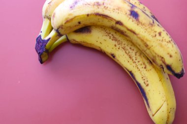 Birkaç olgunlaşmış muz katı pembe bir yüzey üzerinde yatar. Sarı kabuk kahverengi noktalarla kaplıdır ve gövdesi kararmıştır. Meyveler fırın ya da meyve suyu için hazır..