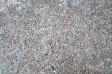 Küçük taşlar ve düzensizliklerle kaplı sert beton yüzey bir güç ve endüstriyel karakter hissi yaratıyor. Zar zor belli olan gri renk dokuya derinlik katar.