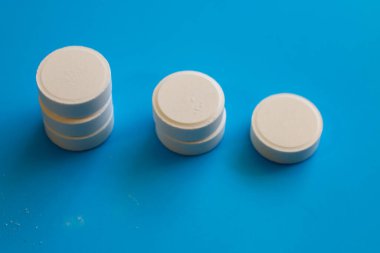 Farklı yükseklikte üç adet beyaz yuvarlak tablet parlak mavi arka planda düzenlenmiştir. Dozaj ya da azaltma kavramını gösteren tıbbi hazırlıklar.