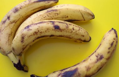 Kahverengi benekli üç olgun sarı muz parlak sarı bir zemin üzerinde uzanır, kabukları kararmaya başlar, tatlılığı işaret eder..