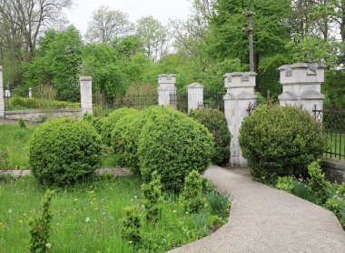 Yeşil çalılar ve taş çit direklerinin arasında gri bir taş yol var. Ağaçlar ve çimenler Ukrayna 'da bulutlu bir gökyüzü altında peyzaj tasarımı yapar..
