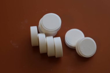 Görüntü koyu kahverengi arka planda iki beyaz yuvarlak tablet grubunu gösteriyor. Bir grup bir sütuna dizilmiş dört tabletten oluşur, diğer üçü yan yana dizilmiştir..