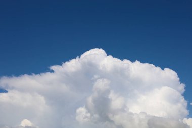 Gökyüzünün zengin mavi rengi, alttaki beyaz kümülüs bulutlarıyla çelişen resmin çoğunu kaplar. Güneş ışığı bulutların hacmini vurgular.