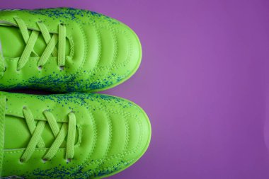 Yukarıdan bakıldığında, mor arka planda mavi benekli parlak yeşil futbol kramponları görülebilir. Bağcıklar bağlanmış, görüntünün sol tarafında yer alıyor..
