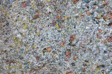 Yakın plan, kahverengi, siyah ve sarı minerallerin yer aldığı gri bir taşın kaba yüzeyini gösteriyor. Taşın gözenekli dokusu doğal kökenini gösteriyor..