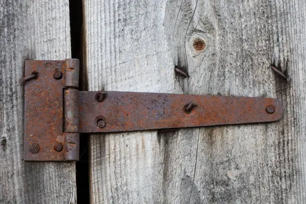 Paslı bir metal kapı menteşesi eski bir ahşap yüzeye bağlıdır. Aşınmış, hasarlı yapısı ahşabın dokusuyla çelişiyor..
