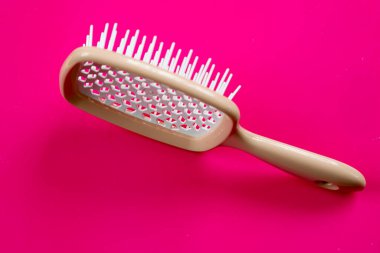 Canlı pembe bir arka planda kendine özgü bir tasarımı olan modern bir masaj fırçası. Kolayca ve nazikçe çözer, saç sağlığı ve güzelliği teşvik eder..