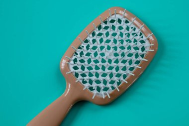 Beyaz tüylü, modern bir bej masaj saç fırçası canlı bir turkuaz arka planda duruyor. Minimalist ve şık bir kompozisyon oluşturuyor..