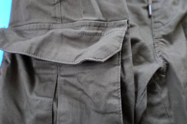 Yük pantolonu cebine yakın çekim ya da zeytin rengi askeri kıyafetler. Görüntü dayanıklı kumaş dokusu ve işlevsel detaylara odaklanır.