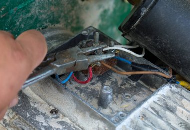 El ele tutuşan kerpeten, tozlu bir mekanizma üzerindeki eski metal terminallere renkli kablolar bağlamak ya da bağlamak için elektrik kablolarıyla çalışır. Bu resim elektrik bağlantılarını tamir etme veya kurma sürecini vurgular, 