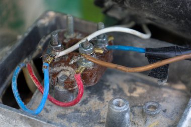 Yakın çekim, toz ve kirle kaplı bir mekanizma üzerindeki metal terminallere bağlı renkli kablolarla elektrik kablolarını ortaya çıkararak teknik görünüm ve ekipman operasyonunu vurguluyor..