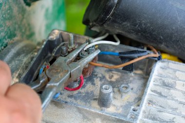 Elektrik kabloları ve terminallerle çalışan, kıskaçları motora bağlanmak için kullanan yakın plan eller. Bu çekim, kabloların ve araçların detaylarını vurgulayarak, ekipmanların onarımı veya bakımı sürecini iletir..