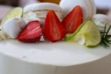 Süslü bir pasta beyaz kremayla süslenir taze çilekler, limon dilimleri, kremalar ve badem kurabiyeleriyle. Bu tatlı şenlikli ve iştah açıcı görünüyor. Özel durumlar için ideal..