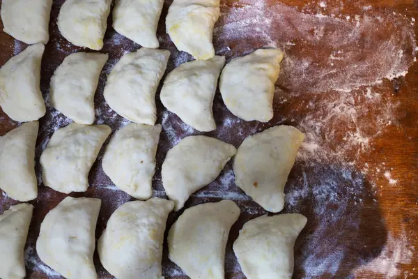 Yeni yontulmuş varenky sıraları, un tozlu, ahşap bir tahtaya uzanmış, ev yapımı pişirme sürecini sergiliyor. Bu Ukrayna mutfağının gelenek ve samimiyetini somutlaştırır..