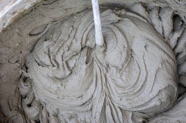 Büyük bir konteynırda, yoğun bir çimento harcı karıştırılıyor, karakteristik dalgalı desenler oluşturuyor. Bu yapı malzemesi kullanıma hazır, dokusu güçlü ve güvenilir duvar ustası veya kaplama için ideal tutarlılığı gösteriyor..