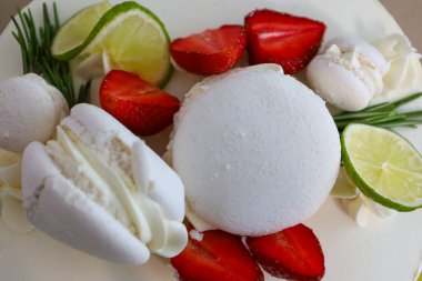 Yakın plan beyaz bir pasta üzerinde nefis dekorasyonlar gösteriyor: taze çilekler, parlak limon dilimleri, narin beyaz kremalar ve yeşil biberiye..
