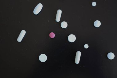 Siyah arkaplandaki renkli hapların ve kapsüllerin dağılması sağlık konusuna görsel bir vurgu yaratıyor. Bu bileşim ilaç ürünlerini, tedaviyi ve tıbbi bakımın önemini sembolize etmektedir..