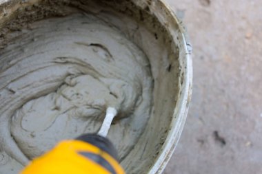 Bir işçi havan topunu elektrikli mikserle karıştırır ve inşaat işi için homojen bir karışım yaratır. Bu süreç, duvarcılık veya kaplama için materyallerin hazırlanmasını gösterir.