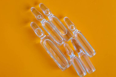 Temiz cam ampuller canlı turuncu bir zemin üzerinde eşit olarak düzenlenerek, minimalist ve keskin bir görüntü oluşturulur. Camdaki ışık yansımaları, tıp, bilim ya da araştırmayı sembolize eden şeffaflıklarını vurgular..