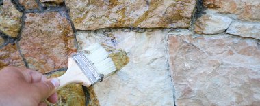 Ön cephe yenileme: bir zanaatkârın eli taş bir duvara özel bir çözüm uygular ve ona taze bir parıltı verir. Bu süreç taşın dokusunu vurgular, görünüşünü daha zengin ve daha iyi korunmuş yapar..