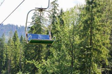 Boş bir sandalye pürüzsüz bir yeşil orman üzerinde süzülüyor, berrak mavi gökyüzünün altındaki görkemli dağların panoramik manzarasını sunuyor, keşif ve macerayı davet ediyor..