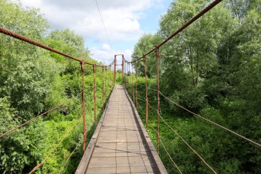 Ahşap güverteli asma köprü yoğun yeşillik boyunca uzanır ve berrak bir gökyüzünün altındaki bilinmeyen mesafeye çıkar. Macerayı ve doğayı keşfetmeyi davet eder..