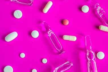 Şeffaf ampuller ve renkli haplar parlak pembe bir arka plana rastgele dağılmış, dinamik bir görsel görüntü yaratıyor. Bu kompozisyon tıbbın önemini ve sağlık mücadelesini sembolize eder..