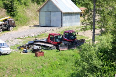 Slavsko, Ukrayna - 13 Temmuz 2025: Binanın önünde iki kırmızı raylı araç, muhtemelen kar tımarcıları veya tomruk makineleri, ve hurda metal yığınları, aktif operasyonları veya atölye çalışmalarını gösteren