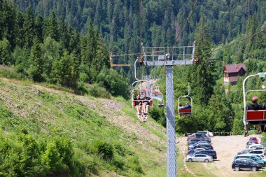 Slavsko, Ukrayna - 13 Temmuz 2025: Yolcular panoramik bir dağ manzarasının keyfini çıkararak yeşil bir ormanın üzerinde bir asansöre biniyorlar. Güneşli bir yaz günü özgürlük ve tazelik hissi verir..