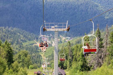 Slavsko, Ukrayna - 13 Temmuz 2025: Kalabalık bir ormanın ve dağ manzarasının üzerinden geçen bir teleferik. Parlak güneş ve yeşil doğa yaz tatili ve seyahat için ideal koşullar yaratır..