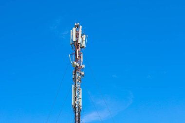 Sayısız anten ve vericiyle donatılmış uzun bir telekomünikasyon kulesi bulutsuz mavi bir gökyüzüne yükseliyor. Çağdaş iletişim teknolojilerini ve altyapısını sembolize ederek, kapsama alanı sağlar..