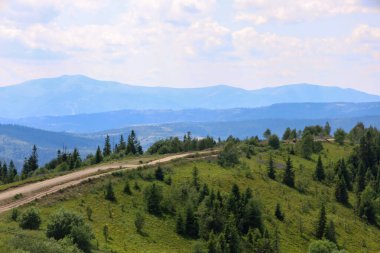 Görkemli bir panoramik manzara dağ yamacı boyunca uzanan toprak bir yol ihtişamlı dağ sıralarının zeminine karşı. Görüntü seyahat ve macera atmosferini mükemmel bir şekilde aktarıyor, doğada keşif ve aktif eğlence için davet ediliyor..