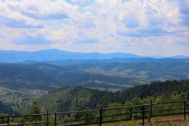 Ormanlar ve dağınık evlerle dolu yeşil vadilere sorunsuzca geçiş yapan görkemli dağ sıralarının panoramik görüntüsü..