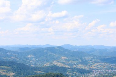 Yoğun ormanlarla kaplı devasa bir dağ sırası ufka doğru uzanır ve orada hafif bir sis bulutuna dönüşür. Görüntü dağların ihtişamını, sükunetini ve doğal güzelliğini gösteriyor.,